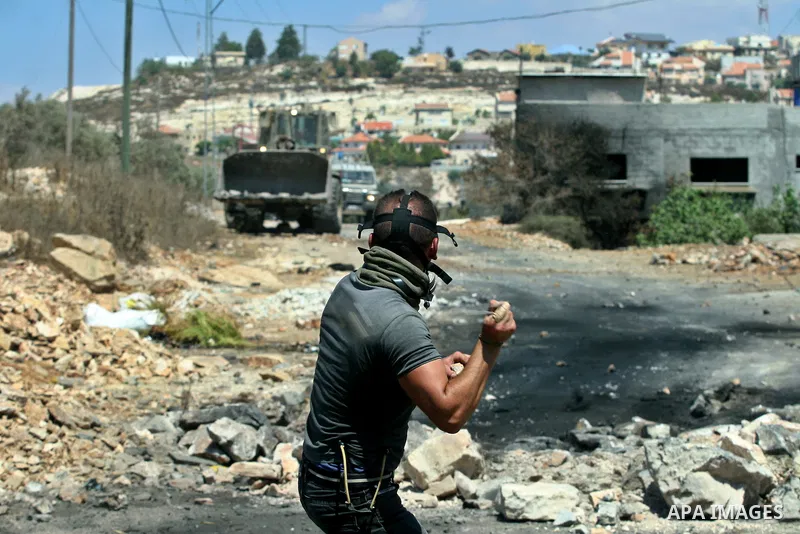 A Palestinian protester throws stones at Israeli bulldozer during a demonstration against the expropriation of Palestinian land by Israel in the village of Kafr Qaddum, near the West Bank city of Nablus, on August 10, 20...