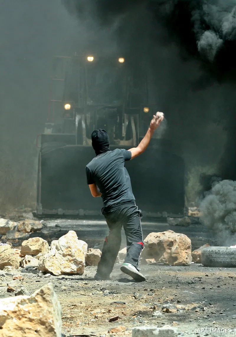 A Palestinian protester throws stones at Israeli bulldozer during a demonstration against the expropriation of Palestinian land by Israel in the village of Kafr Qaddum, near the West Bank city of Nablus, on August 10, 20...
