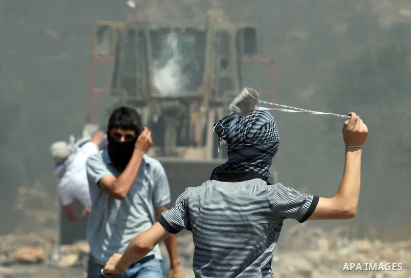 A Palestinian protestor hurls stones using a slingshot at Israeli bulldozer during a demonstration against the expropriation of Palestinian land by Israel in the village of Kfar Qaddum, near the West Bank city of Nablus,...