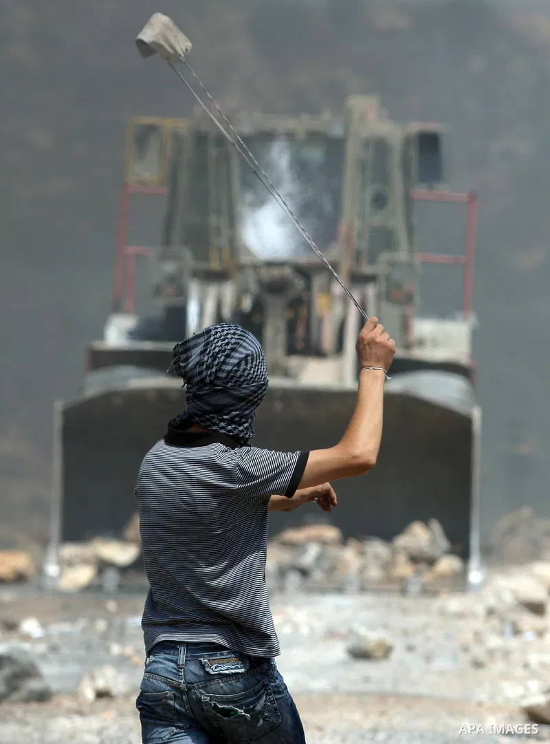 A Palestinian protestor hurls stones using a slingshot at Israeli bulldozer during a demonstration against the expropriation of Palestinian land by Israel in the village of Kfar Qaddum, near the West Bank city of Nablus,...