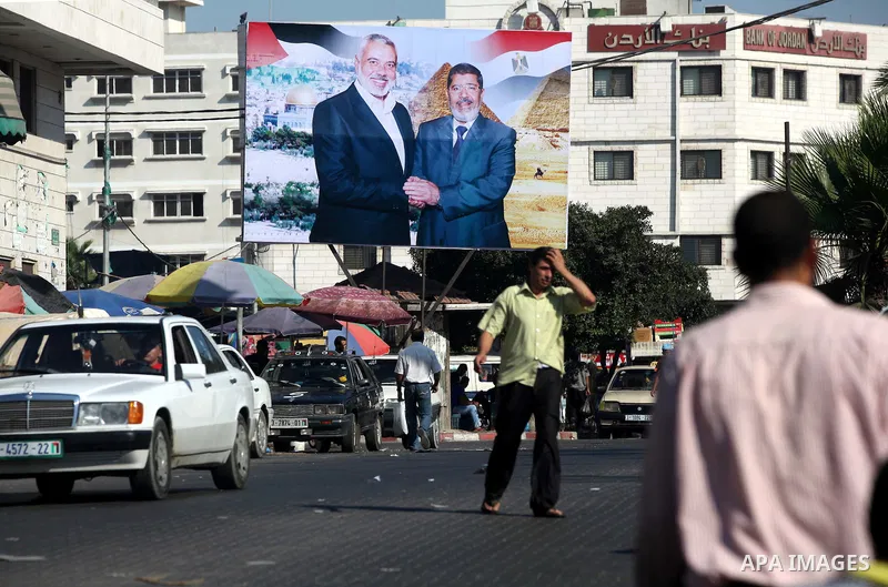 Palestinians walk pass a photograph released by Hamas, Egyptian President Mohammed Morsi, right, meets the Palestinian Prime Minister in Gaza, Ismail Haniyeh, in Gaza city on 18 Aug 2012. Photo by Majdi Fathi