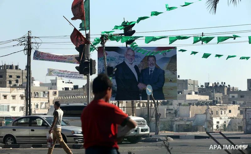 Palestinians walk pass a photograph released by Hamas, Egyptian President Mohammed Morsi, right, meets the Palestinian Prime Minister in Gaza, Ismail Haniyeh, in Gaza city on 18 Aug 2012. Photo by Majdi Fathi