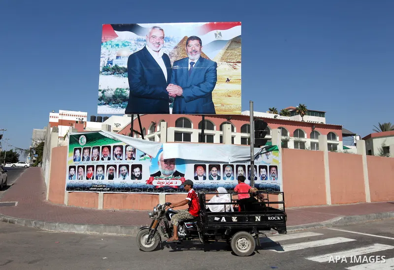 Palestinians walk pass a photograph released by Hamas, Egyptian President Mohammed Morsi, right, meets the Palestinian Prime Minister in Gaza, Ismail Haniyeh, in Gaza city on 18 Aug 2012. Photo by Majdi Fathi