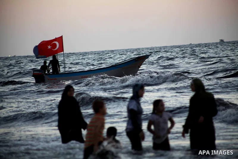 Palestinians hold up Turkish and FC Barcelona soccer team flags on their boat in the sea at Gaza beach during Friday holiday in Gaza city, Aug 24, 2012. Gazans escape to the beach and out from their homes during heat wav...