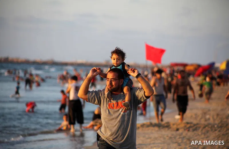 A Palestinian man carries his child at Gaza beach during Friday holiday in Gaza city, Aug 24, 2012. Gazans escape to the beach and out from their homes during heat wave and power outages. Photo by Ashraf Amra
