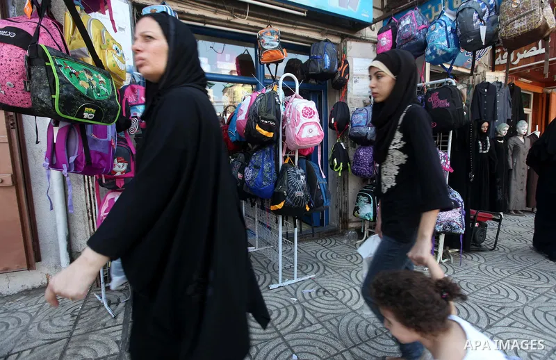 Palestinian women walk past school uniforms and bags displayed at a market in Gaza city on Aug 28, 2012. Next Sunday the First day for the new school year according to Palestinian Ministry of Education in the Gaza strip...