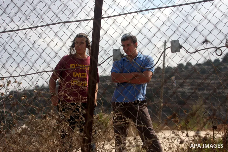 Jewish settlers look at Palestinian villagers inspecting a torched car and anti-Arab graffiti sprayed by vandals believed to be Jewish extremists in the West Bank village of Dura Al-Qara, near Ramallah, on August 29, 201...