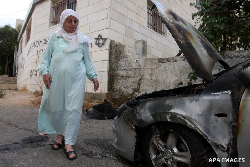 A Palestinian woman inspects a torched car and Hebrew graffiti, that reads "Death to Arabs" and "Migron", referring to the Jewish settlement of Migron, spray painted on the facade of a house by vandals believed to be Jew...