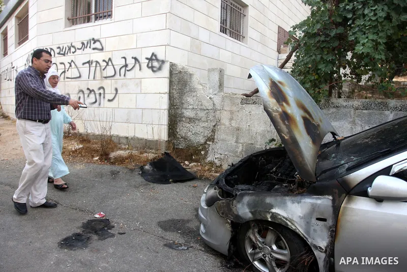 Palestinians inspect a torched car and Hebrew graffiti, that reads "Death to Arabs" and "Migron", referring to the Jewish settlement of Migron, spray painted on the facade of a house by vandals believed to be Jewish extr...
