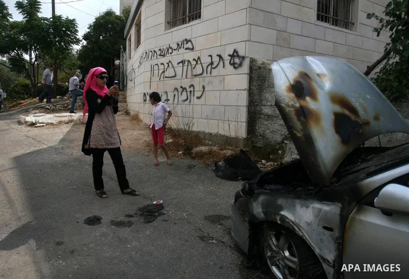 A Palestinian woman takes a picture with her mobile phone of Hebrew graffiti that reads "Death to Arabs" and "Migron", referring to the Jewish settlement of Migron, on the facade of a house by vandals believed to be Jewi...