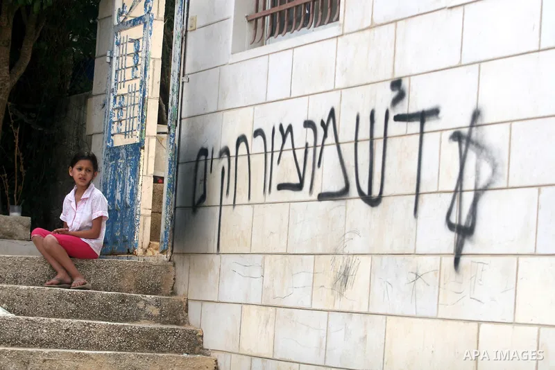 A Palestinian girl looks for Hebrew graffiti that reads "Death to Arabs" and "Migron", referring to the Jewish settlement of Migron, on the facade of a house by vandals believed to be Jewish extremists in the West Bank v...