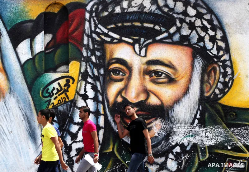 Palestinians walk in front of a mural of the Palestinian Leader Yasser Arafat in Gaza City, on Aug. 29, 2012. A French court has opened an investigation into the death of the late Palestinian leader Yasser Arafat in 2004...