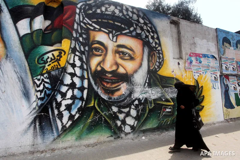 Palestinians walk in front of a mural of the Palestinian Leader Yasser Arafat in Gaza City, on Aug. 29, 2012. A French court has opened an investigation into the death of the late Palestinian leader Yasser Arafat in 2004...