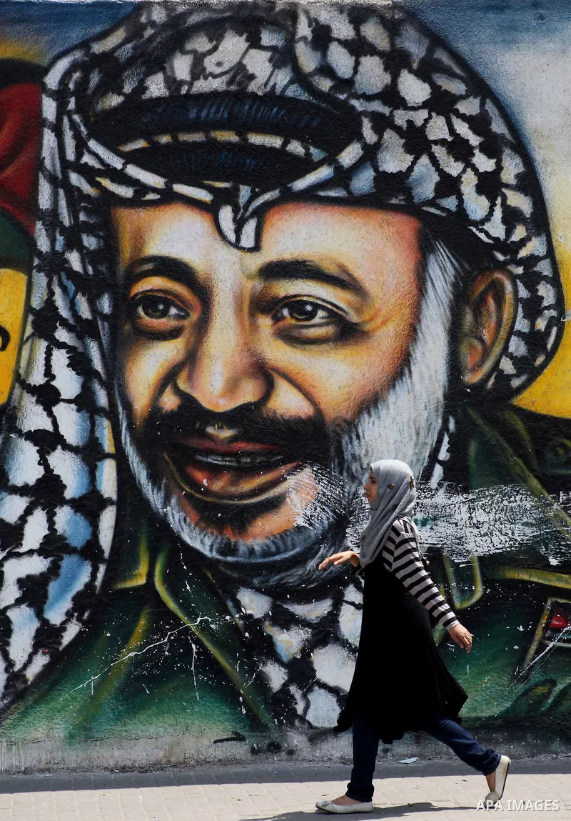 Palestinians walk in front of a mural of the Palestinian Leader Yasser Arafat in Gaza City, on Aug. 29, 2012. A French court has opened an investigation into the death of the late Palestinian leader Yasser Arafat in 2004...