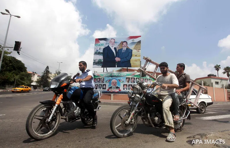 Palestinians ride motorcycles in front of a photograph released by Hamas, Palestinians, Egyptian President Mohammed Morsi, right, meets the Palestinian Prime Minister in Gaza, Ismail Haniyeh, in Gaza city on Aug. 29, 201...