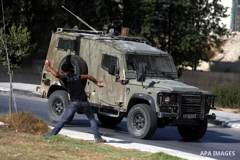 A Palestinian youth throws stones at Israeli troops vehicles as they enter Om al-Sharayet neighborhood, in the West Bank city of Ramallah, Wednesday, Aug 29, 2012. Israeli soldiers raided a store in Om al-Sharayet and le...