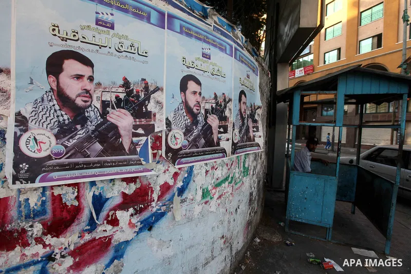 A Palestinian traffic policeman sits next to a picture for the leader in Izz al-Din al-Qassam, the military wing of hamas, the martyr Awad Silmi, on a poster invites Palestinians to view a cinema movie about his life, in...