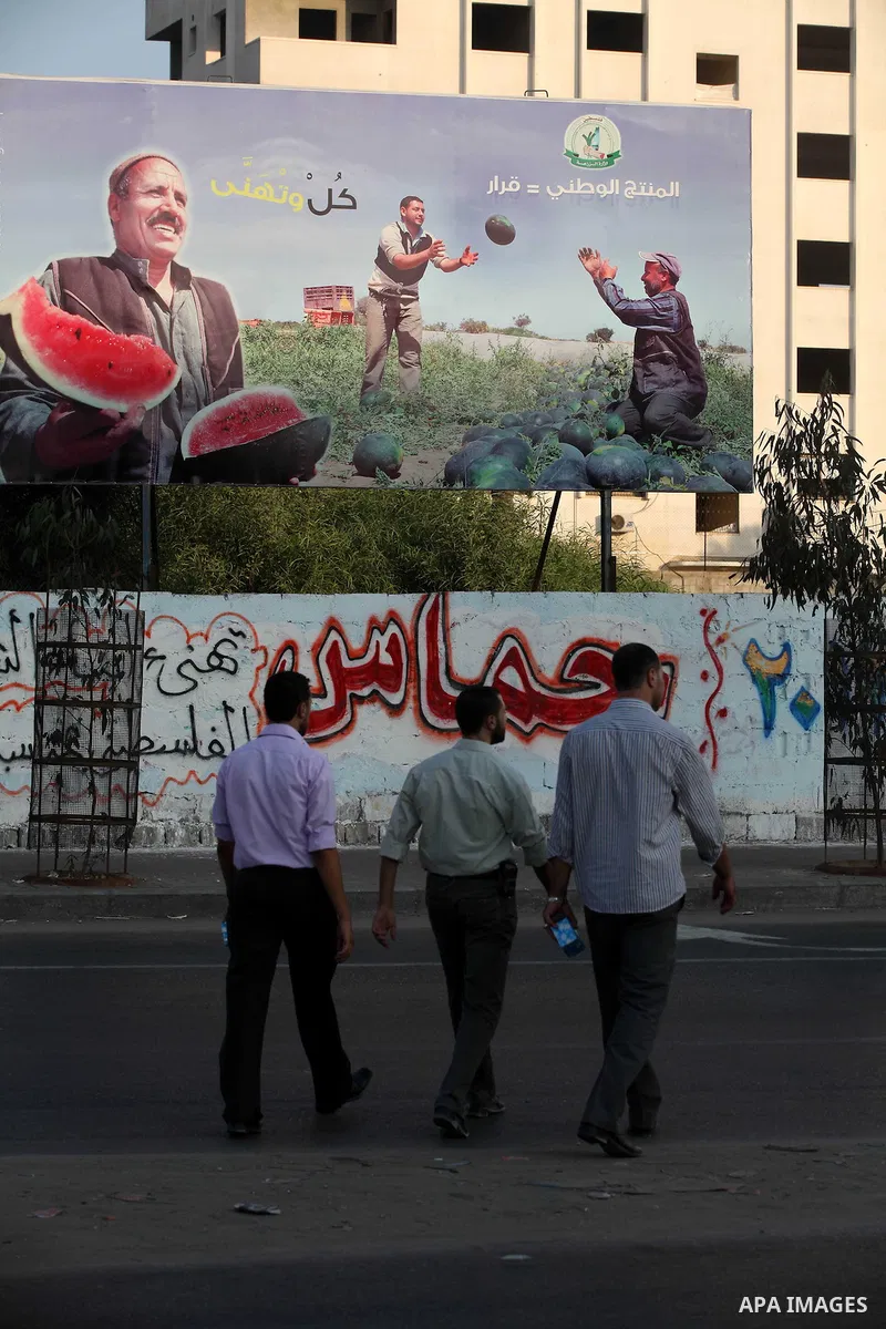 Palestinians walk pass a placard released by Hamas Government reading in Arabic: "National products = Decision", in Gaza city, on Aug 28, 2012. The Ministry of Economy in Gaza started a campaign earlier to support the na...