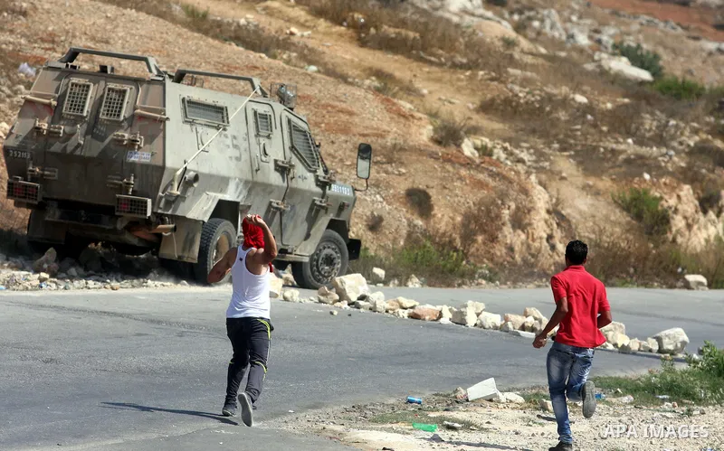 Palestinian demonstrators throws stones towards an Israeli military vehicle during a protest against the confiscation of Palestinian land to expand Jewish settlements in the West Bank village of Nabi Saleh near Ramallah...