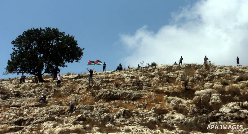 Palestinian protester waves a flag as smoke from tear gas canisters fired by Israeli security forces rises during clashes at a protest against a nearby Jewish settlement, in the West Bank village of Nabi Saleh, near Rama...