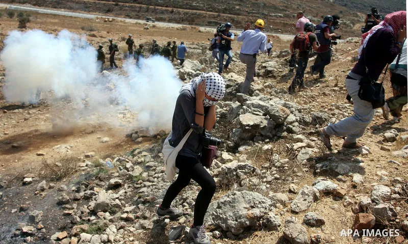 Palestinian protester waves a flag as smoke from tear gas canisters fired by Israeli security forces rises during clashes at a protest against a nearby Jewish settlement, in the West Bank village of Nabi Saleh, near Rama...
