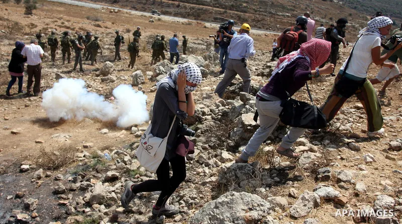 Palestinian protester waves a flag as smoke from tear gas canisters fired by Israeli security forces rises during clashes at a protest against a nearby Jewish settlement, in the West Bank village of Nabi Saleh, near Rama...