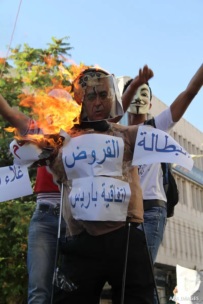 A masked Palestinian demonstrator burns an effigy of Palestinian Prime Minister Salam Fayyad during a protest against economic inequality, in the West Bank city Hebron, Tuesday, Sept 4, 2012. The death of a young Gaza ma...