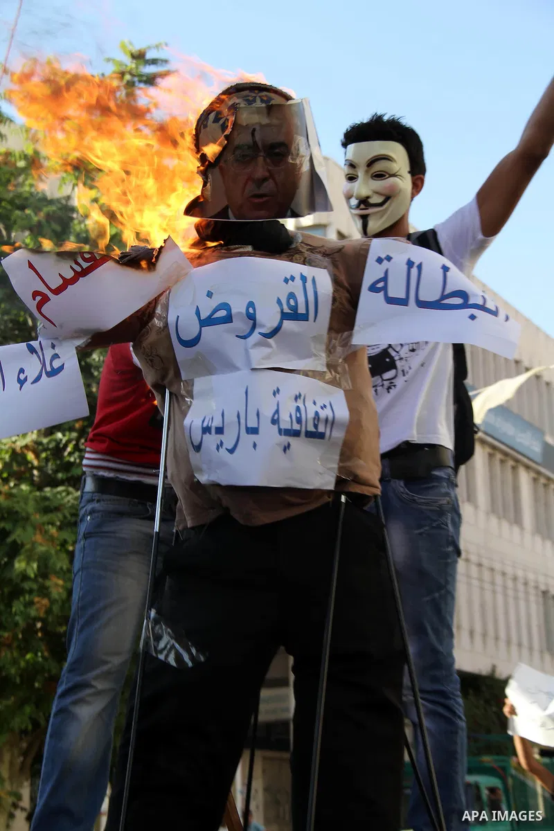 A masked Palestinian demonstrator burns an effigy of Palestinian Prime Minister Salam Fayyad during a protest against economic inequality, in the West Bank city Hebron, Tuesday, Sept 4, 2012. The death of a young Gaza ma...