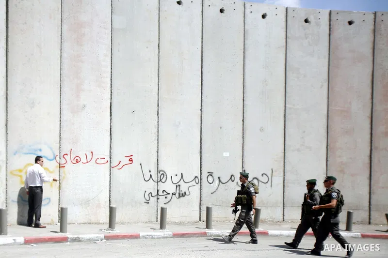 A Palestinian man writes slogans on the separation barrier while Israeli bulldozers continue building in Shu'fat refugee camp in Jerusalem, September 11, 2012. Photo by Mahfouz Abu Turk