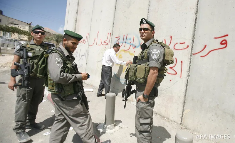 Israeli security forces watch a Palestinian man during writing slogans on the separation barrier while Israeli bulldozers continue building in Shu'fat refugee camp in Jerusalem, September 11, 2012. Photo by Mahfouz Abu T...