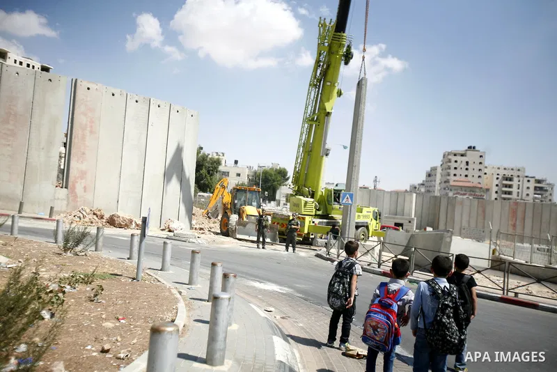 Palestinian students walk pass Israeli bulldozers while continue building the separation barrier in Shu'fat refugee camp in Jerusalem, September 11, 2012. Photo by Mahfouz Abu Turk