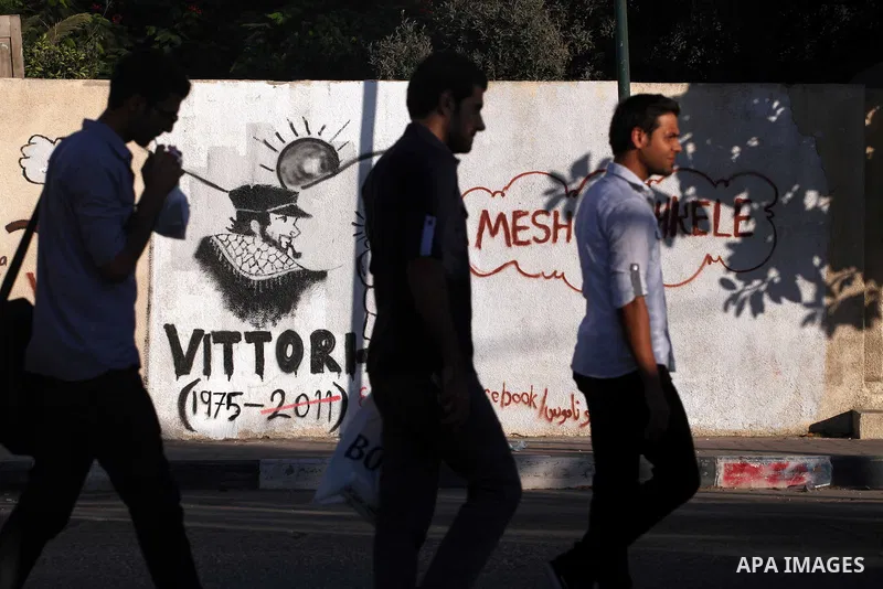 Palestinians walk in front of a wall with graffiti depicting late pro-Palestinian Italian activist Vittorio Arrigoni in Gaza city, Monday, Sept. 17, 2012. A Hamas court convicted four men Monday in the abduction and slay...