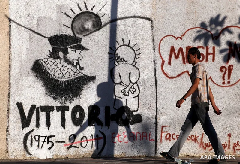 A Palestinian man walks in front of a wall with graffiti depicting late pro-Palestinian Italian activist Vittorio Arrigoni in Gaza city, Monday, Sept. 17, 2012. A Hamas court convicted four men Monday in the abduction an...