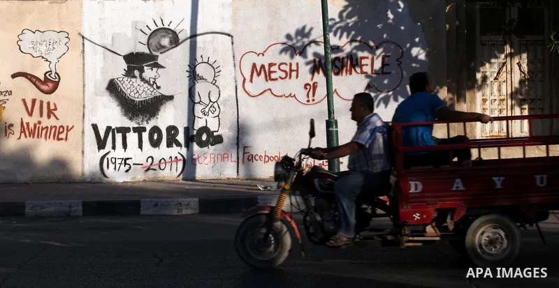 Palestinians ride a motorcycle in front of a wall with graffiti depicting late pro-Palestinian Italian activist Vittorio Arrigoni in Gaza city, Monday, Sept. 17, 2012. A Hamas court convicted four men Monday in the abduc...