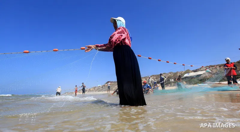 A Palestinian fisherwoman helps her husband to tow his trawl from the sea in Deir al-Balah Palestinian refugee camp, central of Gaza Strip, on September 19, 2012. Photo by Majdi Fathi
