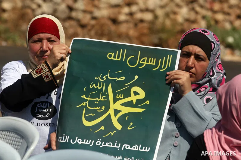 Palestinian woman hold a banner reading in Arabic "Anyone but prophet Muhammad" and shout slogans during a protest in the West Bank town of Ramallah against an anti-Islam movie made in the U.S. and French cartoons said t...