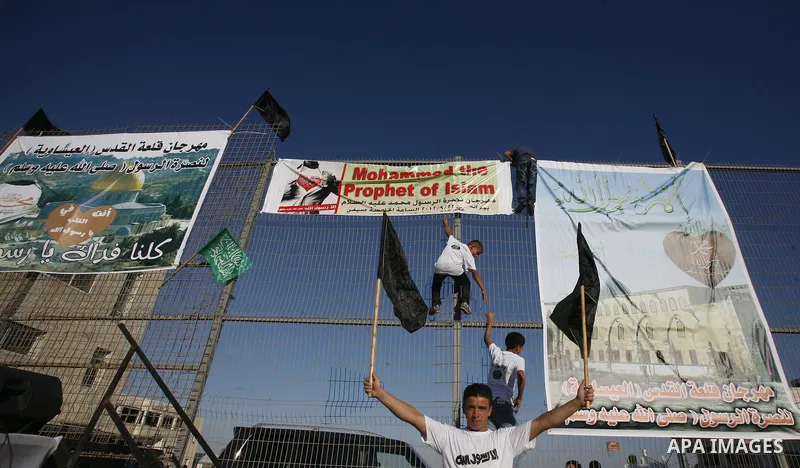 Palestinian boys they place banners on a fence denouncing an US-produced amateur film mocking Islam's Prophet Mohammed and cartoons published in a French satirical magazine Charlie Hebdo in the Issawiya district of Arab...