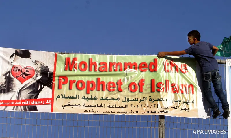 A Palestinian boy climbs a fence during a gathering denouncing an US-produced amateur film mocking Islam's Prophet Mohammed and cartoons published in a French satirical magazine Charlie Hebdo, in the Issawiya district of...