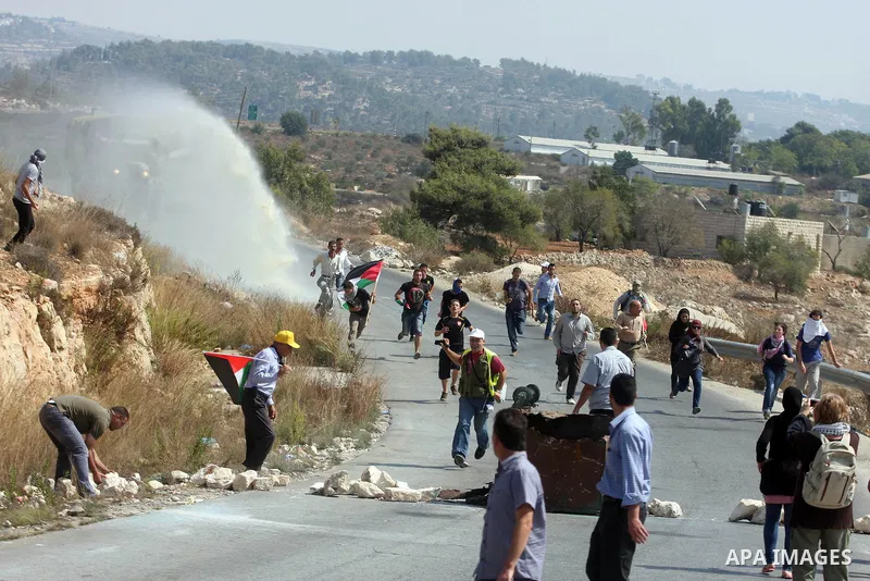 Palestinian protesters run away from a water canon used by Israeli troops to disperse protesters during a weekly protest against the expansion of the nearby Jewish settlement of Halamish, in the West Bank village of Nabi...