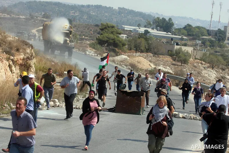 Palestinian protesters run away from a water canon used by Israeli troops to disperse protesters during a weekly protest against the expansion of the nearby Jewish settlement of Halamish, in the West Bank village of Nabi...