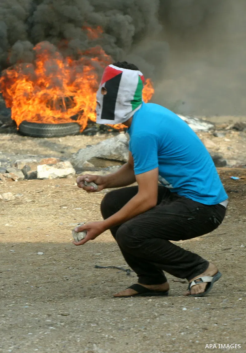 A Palestinian protester wearing a national flag mask throws stones towards Israeli soldiers during a demonstration in the village of Kfar Qaddum near the occupied West Bank city of Nablus on september 29, 2012 in support...