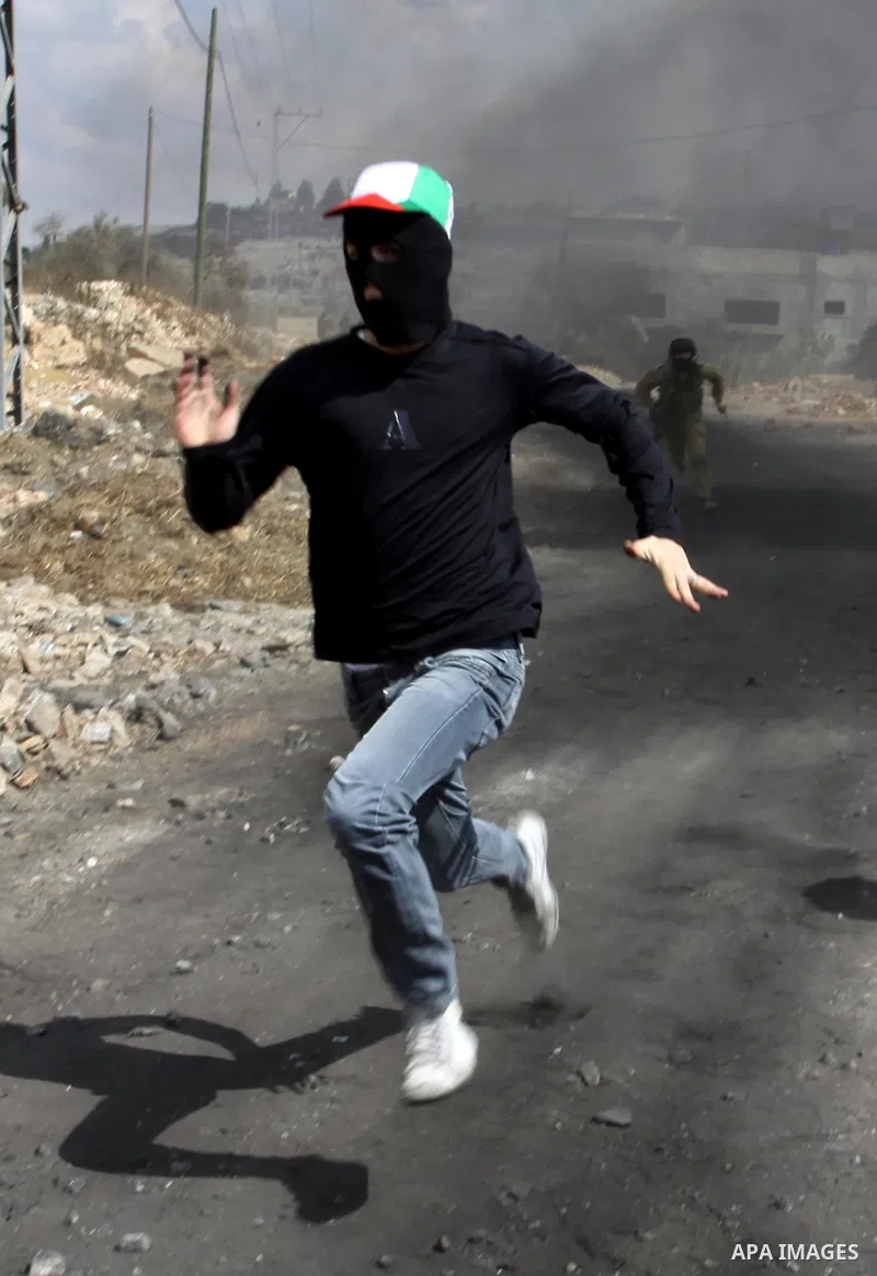 A masked Palestinian protester runs near an Israeli soldier during clashes following a demonstration against the expropriation of Palestinian land by Israel in the village of Kafr Qadum in the occupied West Bank on Octob...