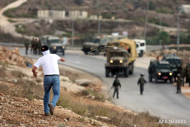 A Palestinian protester hurls stones at Israeli soldiers during a weekly protest against the expansion of the nearby Jewish settlement of Halamish, in the West Bank village of Nabi Saleh near Ramallah, Friday, Oct 5, 201...