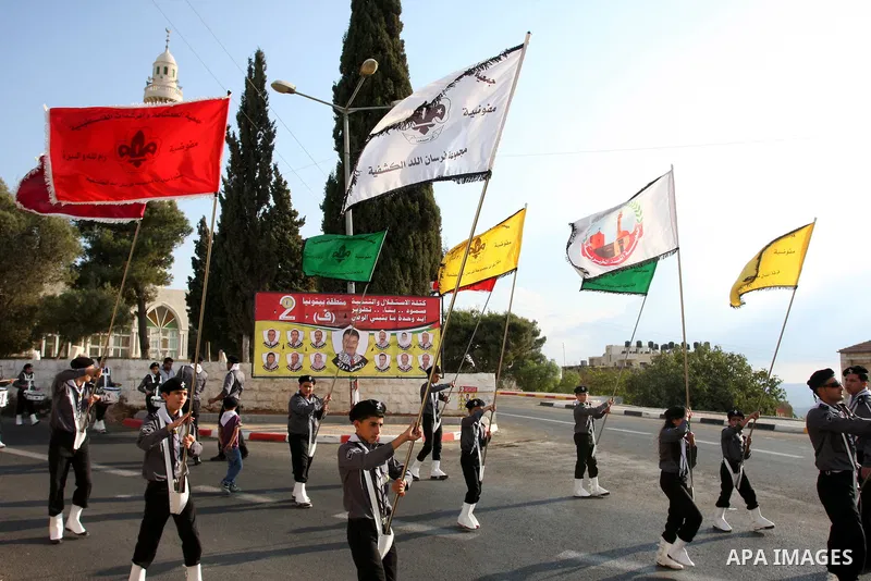 Palestinian Youth holds national flags as he walks past an electoral poster displaying portraits of candidates running for municipal elections on October 6, 2012 in the West Bank city of Ramallah. Campaigning has started...