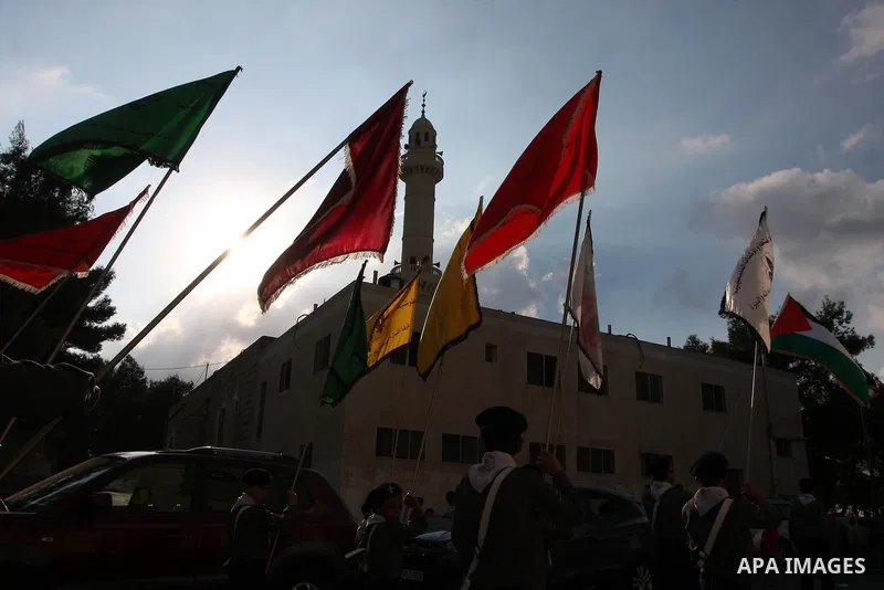 Palestinian Youth holds national flags as he walks past an electoral poster displaying portraits of candidates running for municipal elections on October 6, 2012 in the West Bank city of Ramallah. Campaigning has started...