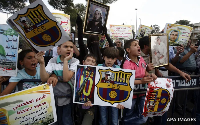 Families of Palestinian prisoners in Israeli jails hold their portraits and placards, bearing a portrait of Israeli soldier Gilad Shalit on the emblem of Spanish FC Barcelona football club, during a demonstration outside...