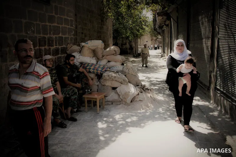 A Syrian woman carries her and walks past members of Free Syrian Army in the old city of Aleppo, September 03 2012. Photo by Ahmed Deeb