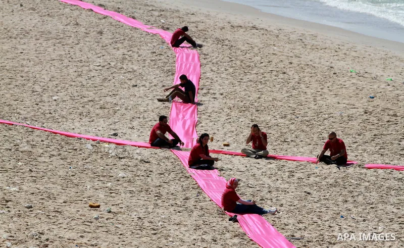 Palestinian youths sit on a beach in Gaza City near a pink ribbon as part of the Breast Cancer Awareness campaign on October 10, 2012. Photo by Majdi Fathi