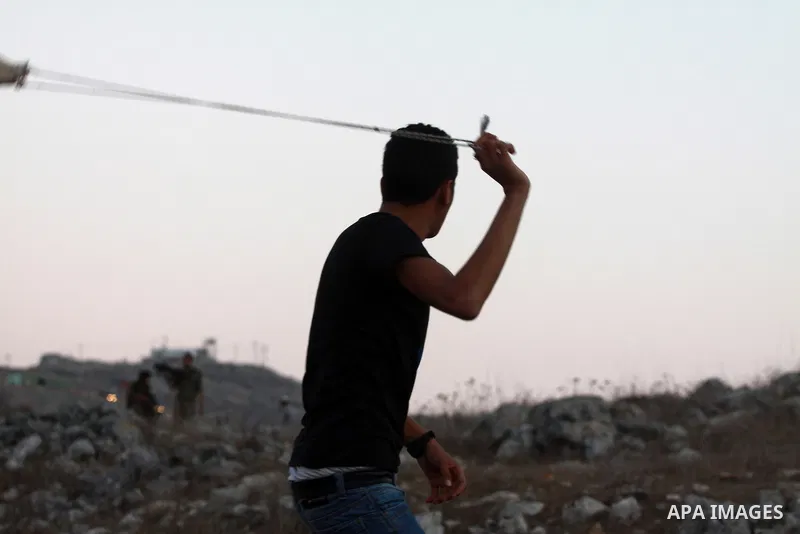 A Palestinian youth throws stones toward Jewish settlers during clashes on October 10, 2012. Over 100 olive trees belonging to Palestinians in a West Bank village have been found uprooted, its mayor said, blaming local J...
