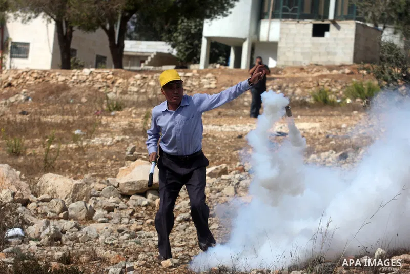 A Palestinian protester stands near cloud of tear gas during a weekly protest against the expansion of the nearby Jewish settlement of Halamish, in the West Bank village of Nabi Saleh, near Ramallah, Friday, Oct 12, 2012...